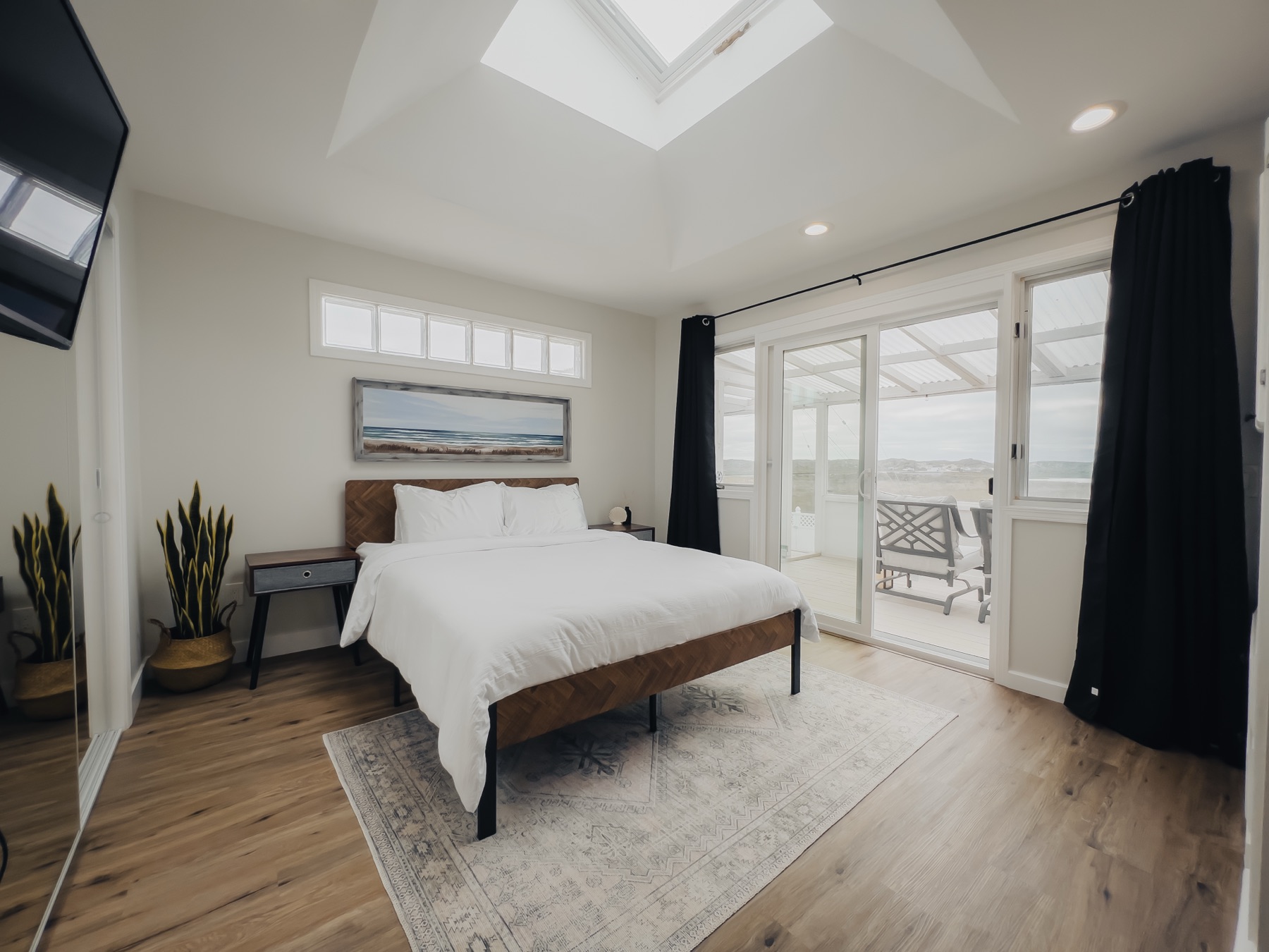 A bright, comfortable resident bedroom with coastal artwork, a skylight, and doors opening onto a sunroom